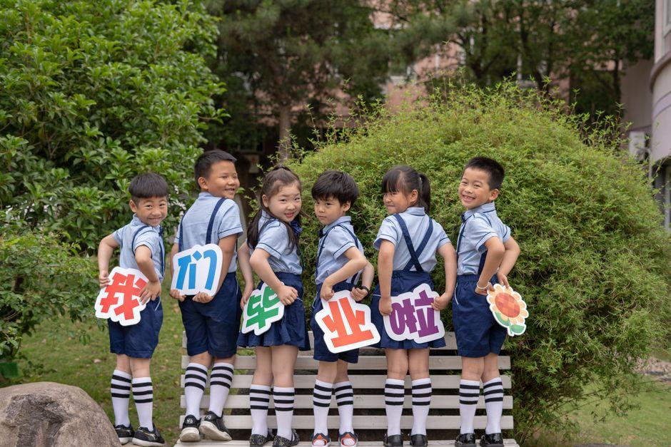 Group of children in uniform holding colorful signs, celebrating graduation outdoors.